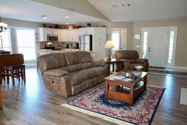 living room with lofted ceiling, dark hardwood / wood-style floors, and an inviting chandelier