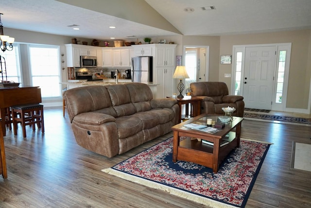 living room featuring dark hardwood / wood-style floors, a textured ceiling, an inviting chandelier, and vaulted ceiling