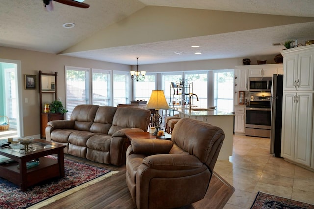 living room featuring sink, vaulted ceiling, ceiling fan with notable chandelier, and a textured ceiling