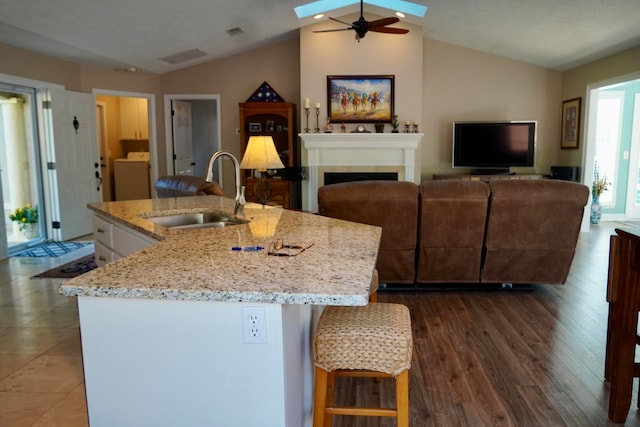 kitchen with washer / clothes dryer, vaulted ceiling with skylight, sink, and a kitchen island with sink