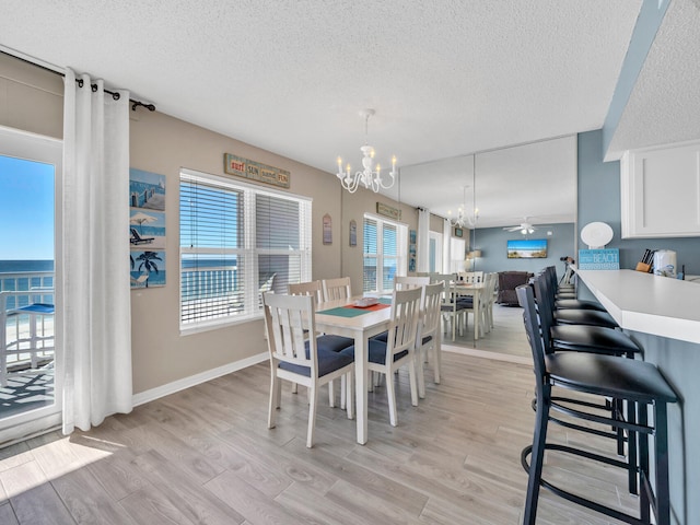 dining area featuring a textured ceiling, ceiling fan with notable chandelier, a water view, and light hardwood / wood-style floors