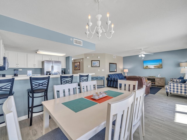 dining space with a textured ceiling, ceiling fan with notable chandelier, and light hardwood / wood-style flooring