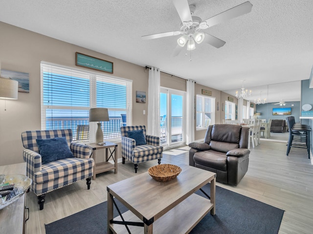 living room with a textured ceiling, light hardwood / wood-style floors, and ceiling fan with notable chandelier