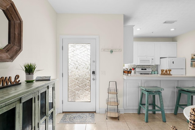 kitchen featuring light tile patterned flooring, white cabinetry, decorative backsplash, a breakfast bar, and white appliances