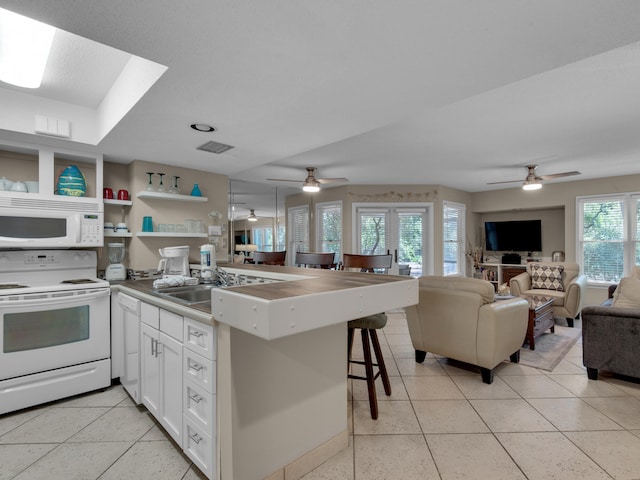 kitchen featuring a wealth of natural light, white appliances, a breakfast bar, and white cabinets