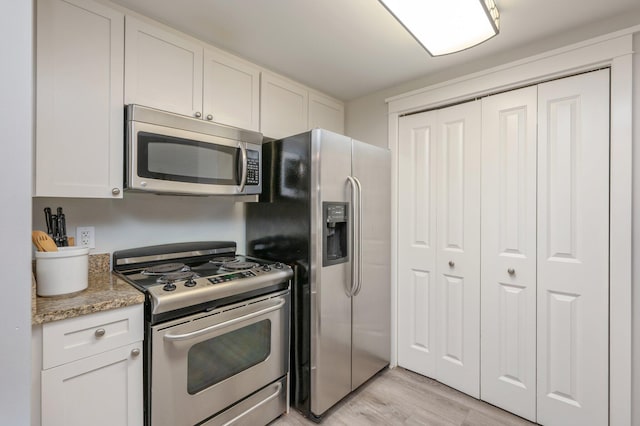 kitchen with white cabinetry, light hardwood / wood-style flooring, stainless steel appliances, and light stone counters