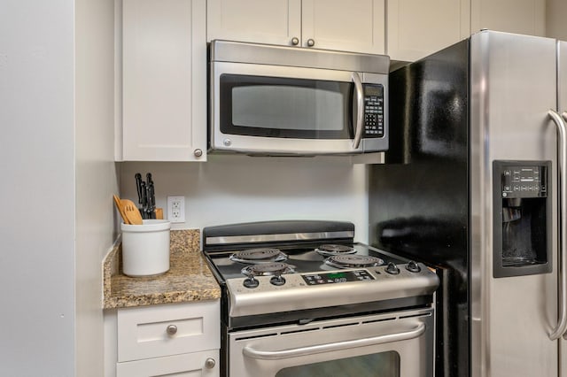 kitchen featuring stainless steel appliances, white cabinetry, and dark stone counters
