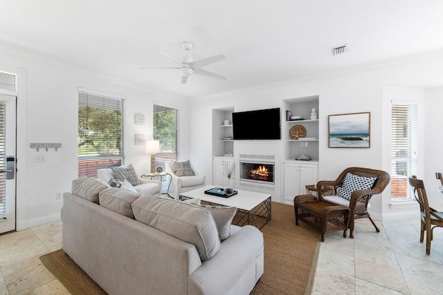 living room featuring built in shelves, ceiling fan, plenty of natural light, and a tiled fireplace