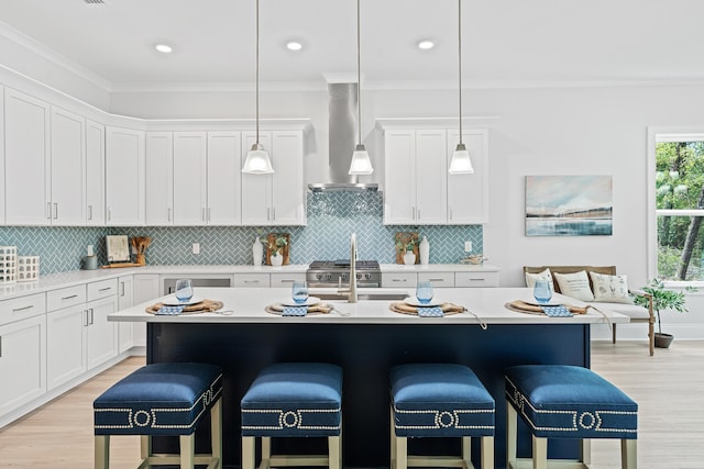 kitchen with a kitchen bar, ornamental molding, hanging light fixtures, wall chimney range hood, and a kitchen island with sink