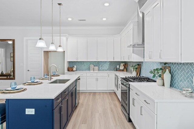 kitchen featuring stainless steel appliances, pendant lighting, white cabinets, wall chimney range hood, and sink