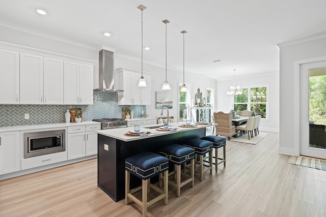 kitchen with wall chimney exhaust hood, stainless steel appliances, a center island with sink, white cabinetry, and sink