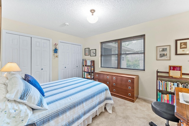 bedroom with a textured ceiling, light colored carpet, and multiple closets