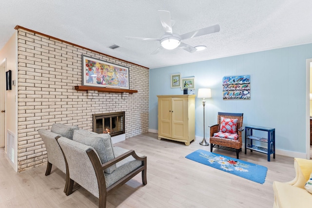 living room featuring a brick fireplace, light hardwood / wood-style flooring, ceiling fan, ornamental molding, and a textured ceiling