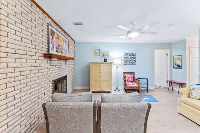 living room featuring a fireplace, a textured ceiling, light wood-type flooring, and ceiling fan