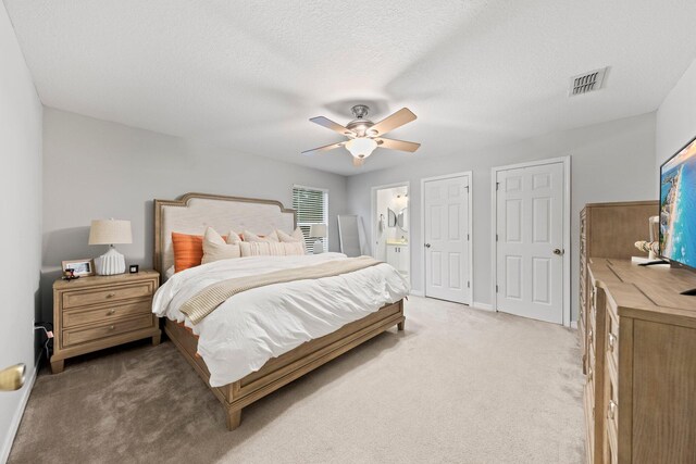 bedroom featuring ensuite bathroom, ceiling fan, a textured ceiling, and light colored carpet