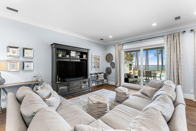 living area with baseboards, crown molding, visible vents, and wood finished floors