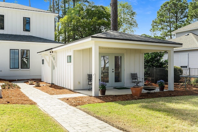 exterior space featuring a shingled roof, french doors, fence, a yard, and board and batten siding