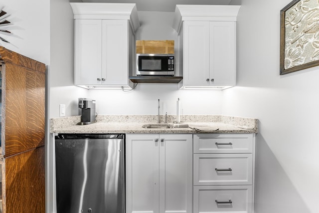 kitchen with appliances with stainless steel finishes, a sink, light stone counters, and white cabinets