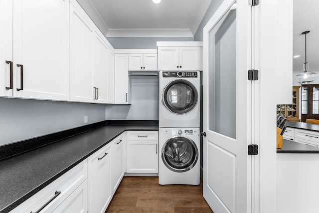 clothes washing area featuring cabinet space, dark wood-style floors, crown molding, and stacked washer and clothes dryer