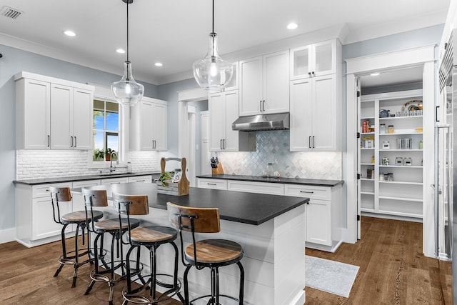 kitchen featuring a breakfast bar area, dark countertops, visible vents, a sink, and under cabinet range hood