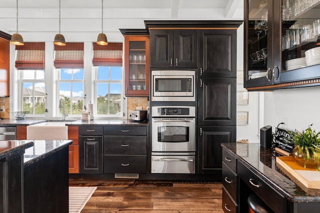 kitchen with appliances with stainless steel finishes, dark hardwood / wood-style floors, pendant lighting, and dark stone countertops