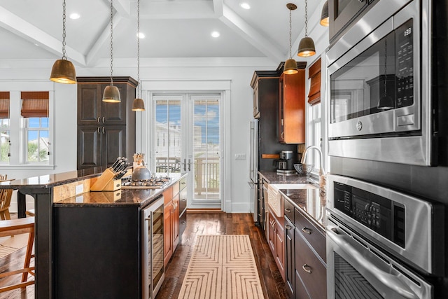 kitchen with a kitchen breakfast bar, appliances with stainless steel finishes, beverage cooler, a kitchen island, and hanging light fixtures