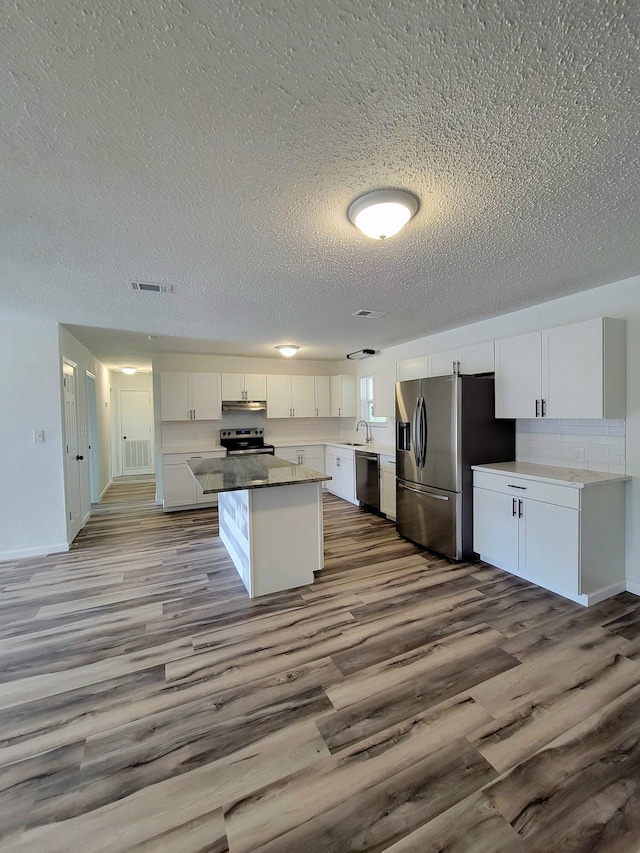 kitchen featuring white cabinets, appliances with stainless steel finishes, a center island, light hardwood / wood-style floors, and a textured ceiling