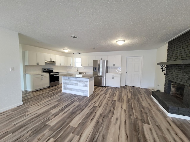 kitchen with a brick fireplace, white cabinetry, stainless steel appliances, and light wood-type flooring