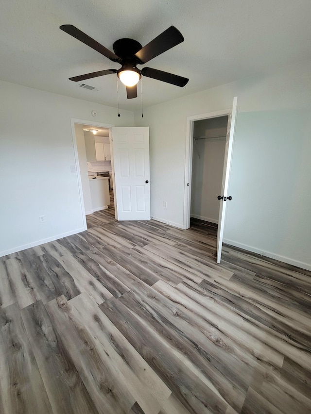 unfurnished bedroom with a closet, ceiling fan, light wood-type flooring, and a walk in closet