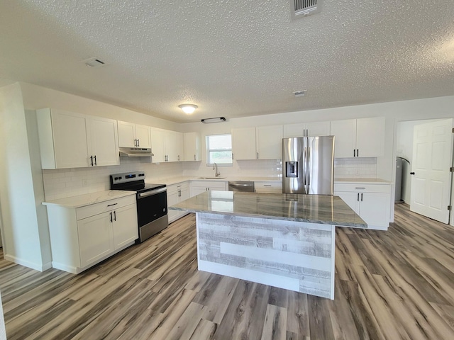 kitchen with white cabinets, a kitchen island, appliances with stainless steel finishes, light wood-type flooring, and light stone counters