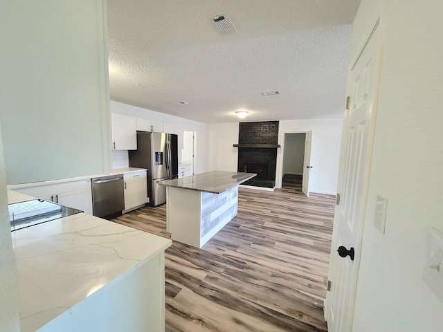 kitchen with a brick fireplace, a textured ceiling, stainless steel appliances, white cabinets, and light hardwood / wood-style floors