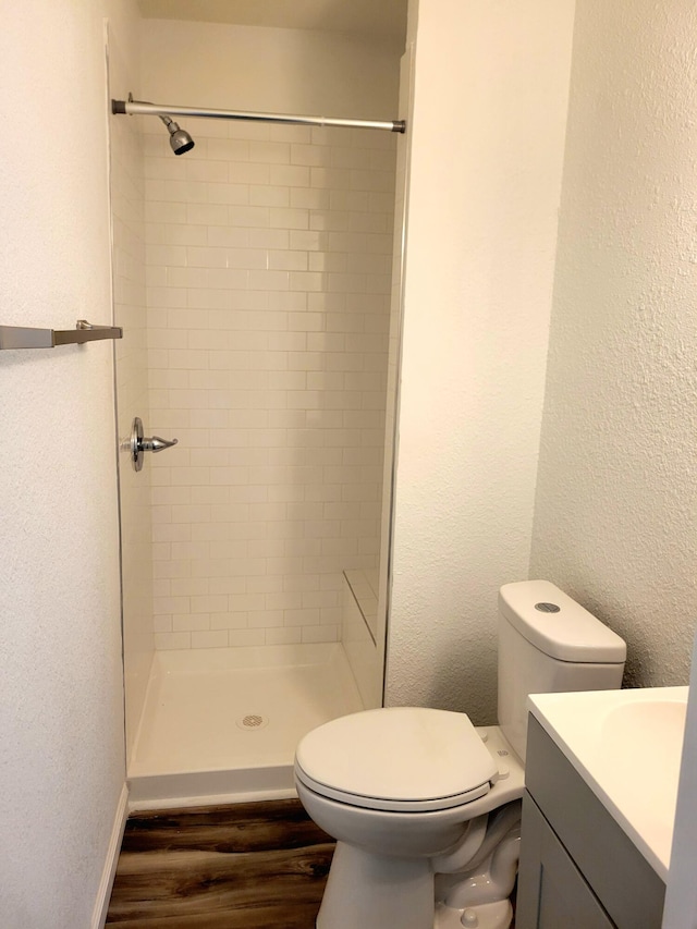 bathroom featuring toilet, hardwood / wood-style floors, vanity, and tiled shower