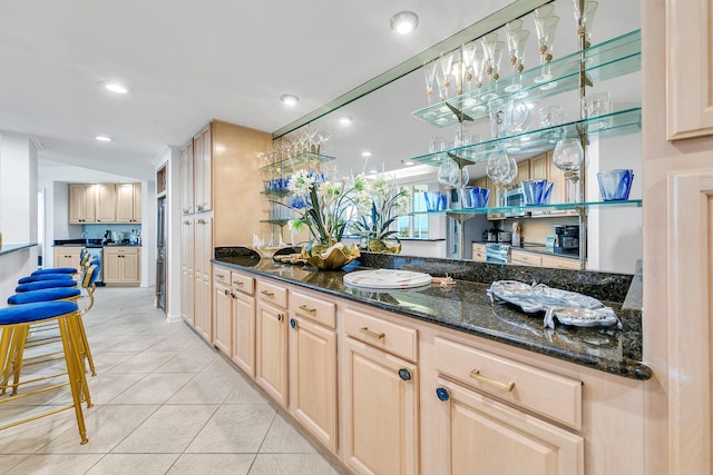 bar featuring light tile patterned floors, light brown cabinets, dark stone counters, and pendant lighting