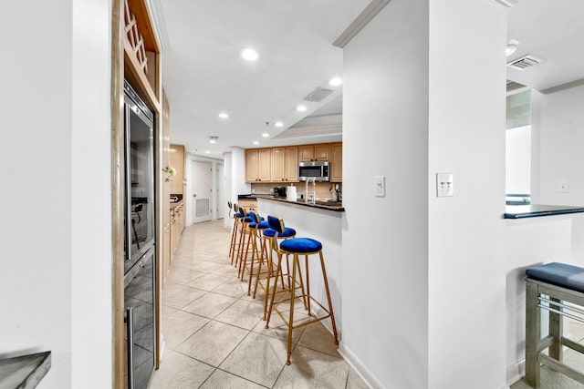 kitchen featuring ornamental molding, a kitchen bar, light tile patterned flooring, tasteful backsplash, and light brown cabinetry