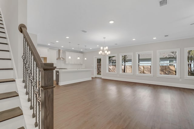 unfurnished living room with hardwood / wood-style flooring, an inviting chandelier, crown molding, and sink