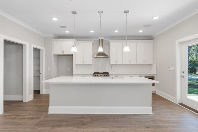 kitchen featuring sink, a center island with sink, a healthy amount of sunlight, and wall chimney range hood