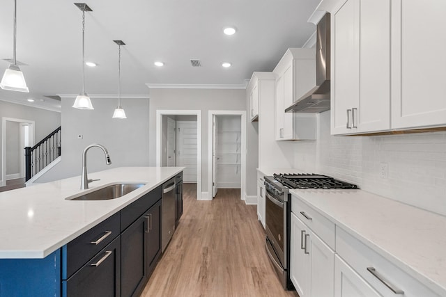 kitchen with hanging light fixtures, an island with sink, stainless steel appliances, and wall chimney range hood