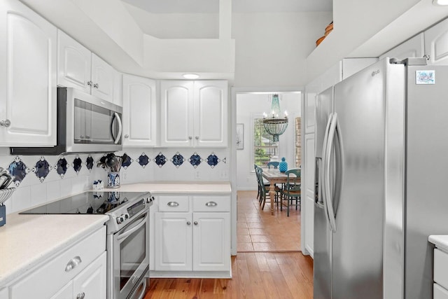 kitchen with light hardwood / wood-style flooring, backsplash, a chandelier, white cabinets, and appliances with stainless steel finishes