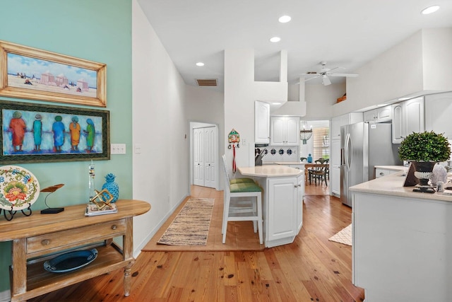 kitchen with a breakfast bar, a high ceiling, white cabinets, light hardwood / wood-style flooring, and stainless steel fridge