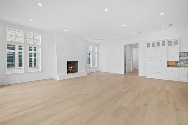 unfurnished living room with plenty of natural light, light wood-type flooring, and ornamental molding