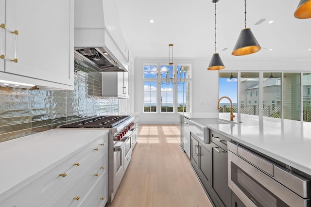 kitchen with white cabinetry, hanging light fixtures, backsplash, custom range hood, and appliances with stainless steel finishes