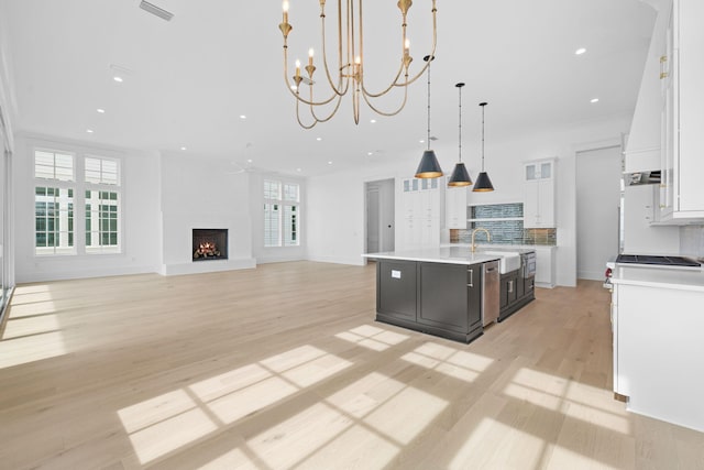 kitchen with white cabinets, a healthy amount of sunlight, an island with sink, and pendant lighting