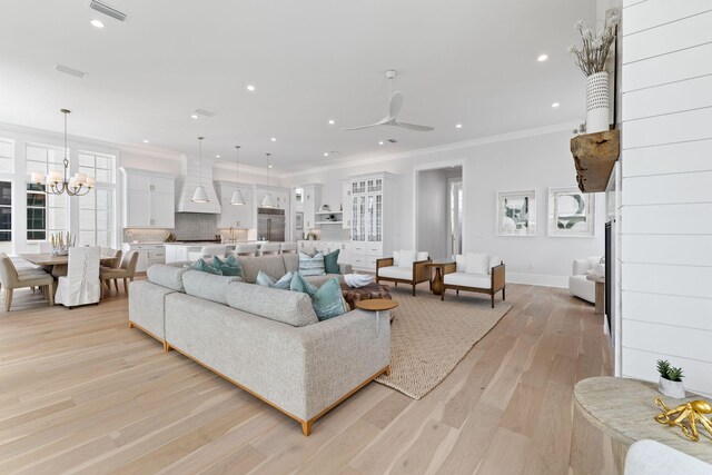 living room with ceiling fan with notable chandelier, ornamental molding, and light hardwood / wood-style flooring