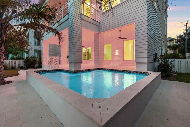 pool at dusk with ceiling fan and a patio