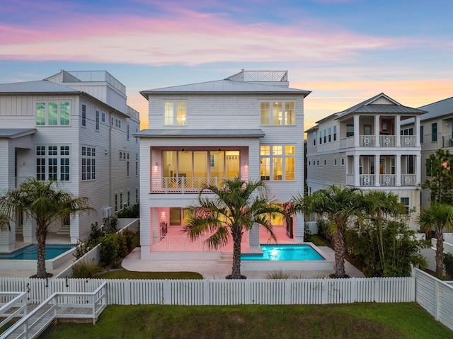 back house at dusk featuring a fenced in pool and a patio area