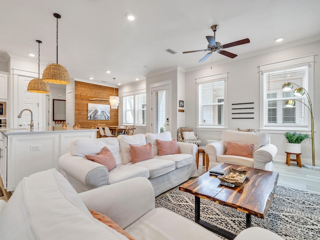 living room featuring wood walls, sink, ceiling fan, ornamental molding, and wood-type flooring