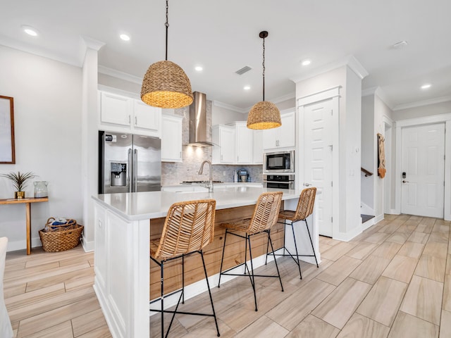 kitchen featuring a breakfast bar, stainless steel appliances, wall chimney range hood, a large island with sink, and pendant lighting