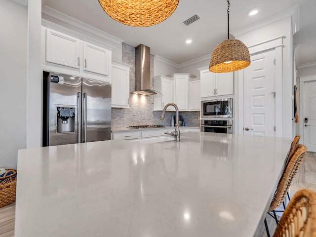 kitchen with wall chimney exhaust hood, stainless steel appliances, crown molding, pendant lighting, and white cabinets