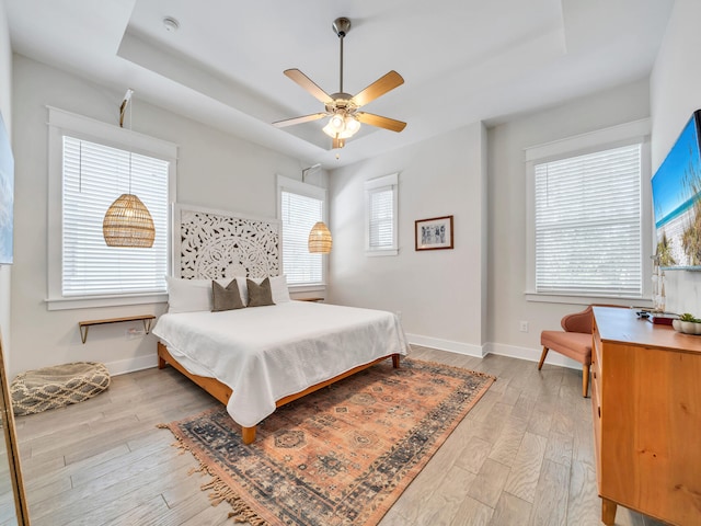 bedroom featuring a raised ceiling, ceiling fan, and light wood-type flooring