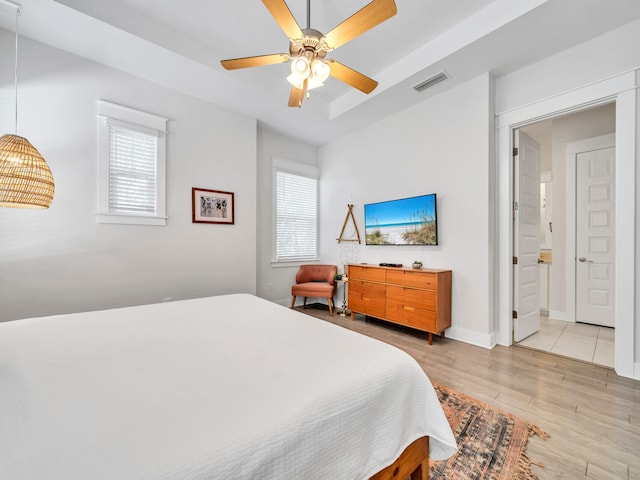 bedroom featuring connected bathroom, light hardwood / wood-style flooring, multiple windows, and ceiling fan